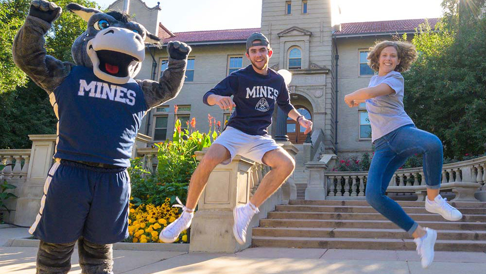 Mines students jumping next to Blaster the Burro in front of Guggenheim Hall